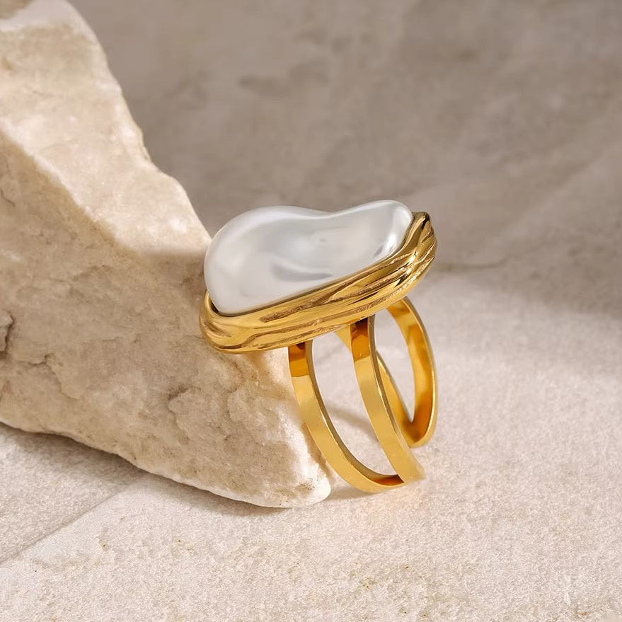 Gold ring with a pearl in a textured beige surface