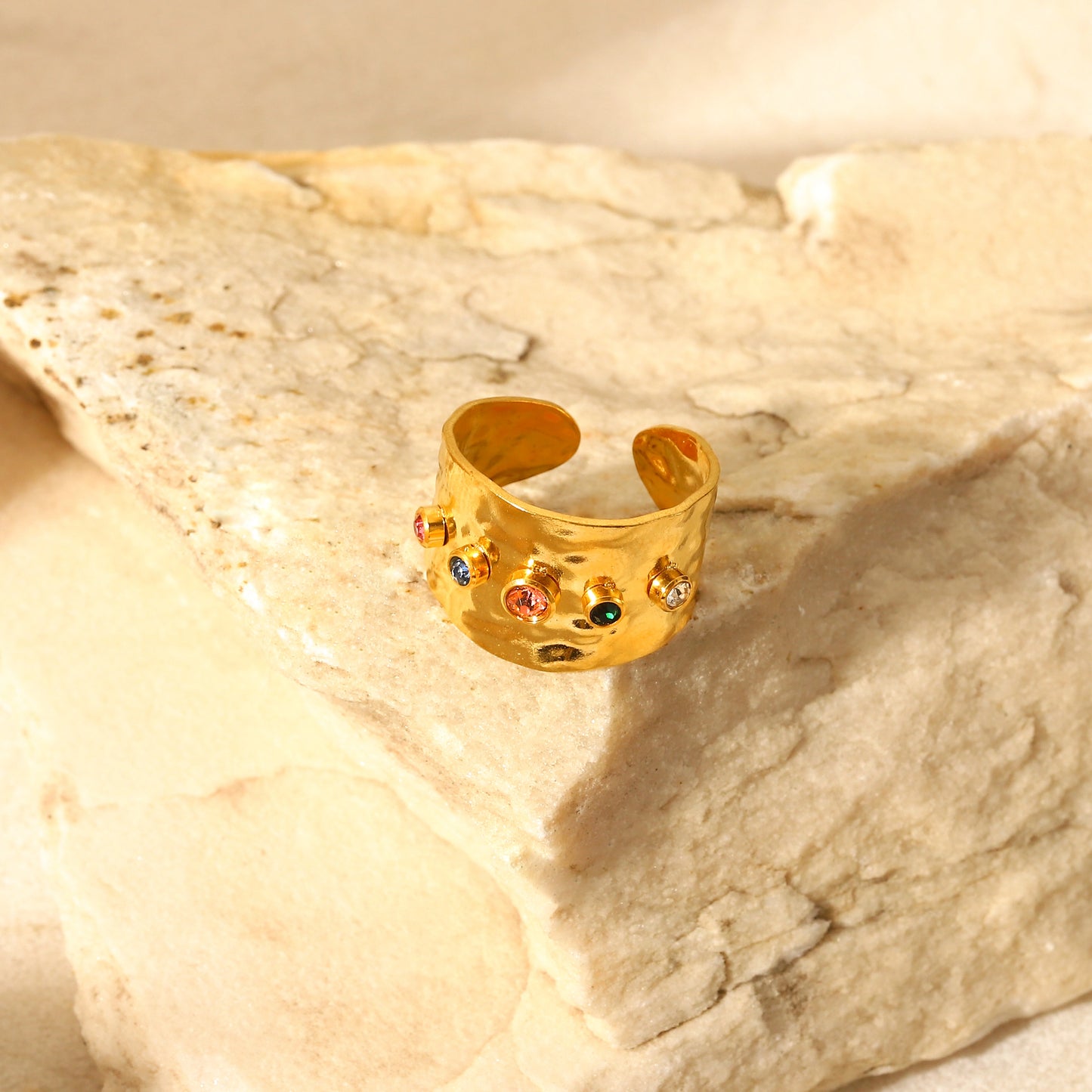 Gold ring with colorful stones on a beige stone surface