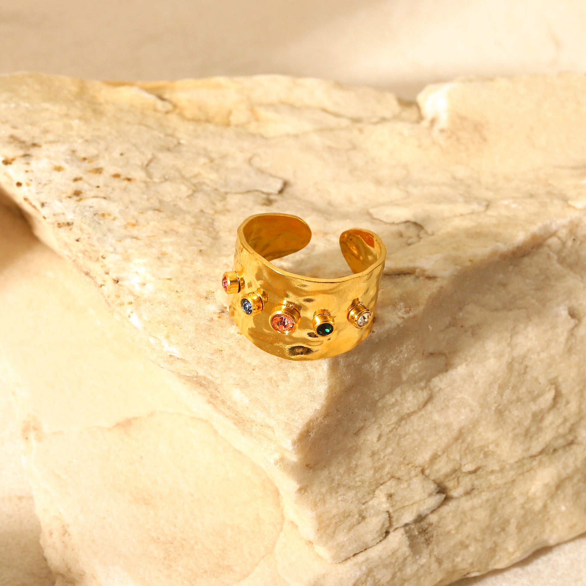 Gold ring with colorful stones on a beige stone surface