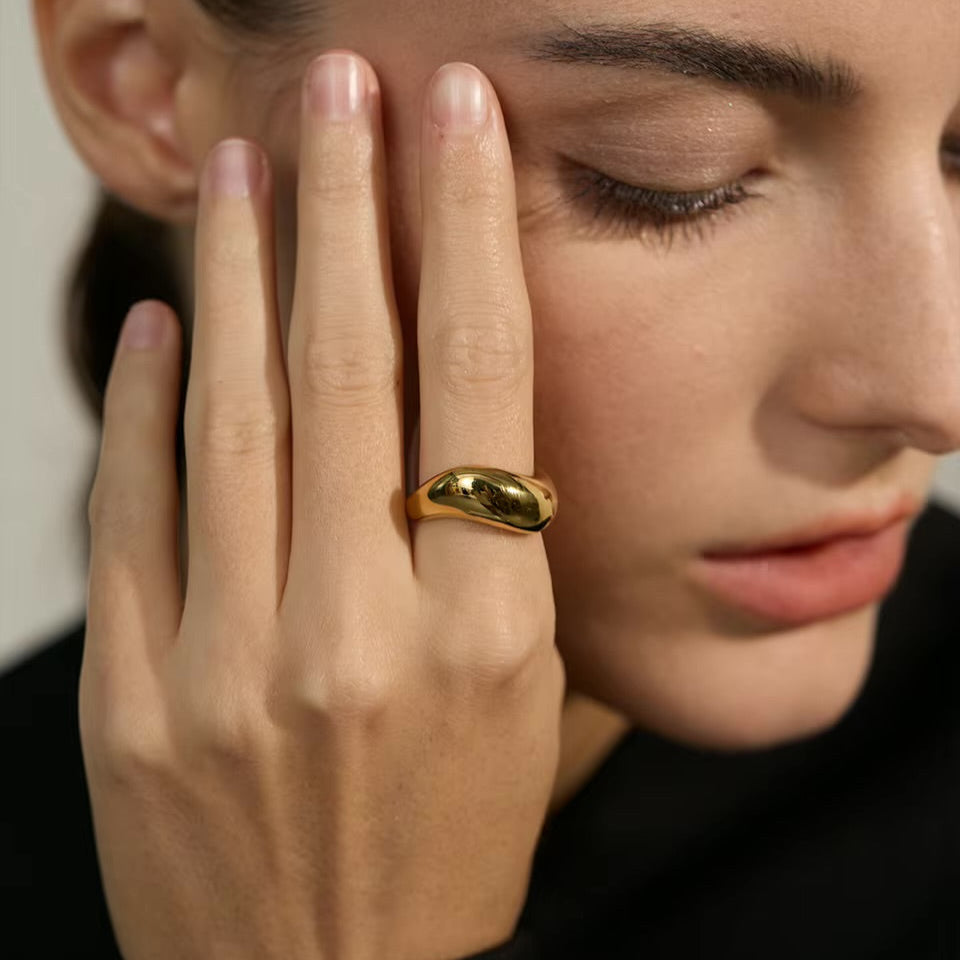 Close-up of a woman's face with a gold ring on her finger, wearing a black top.