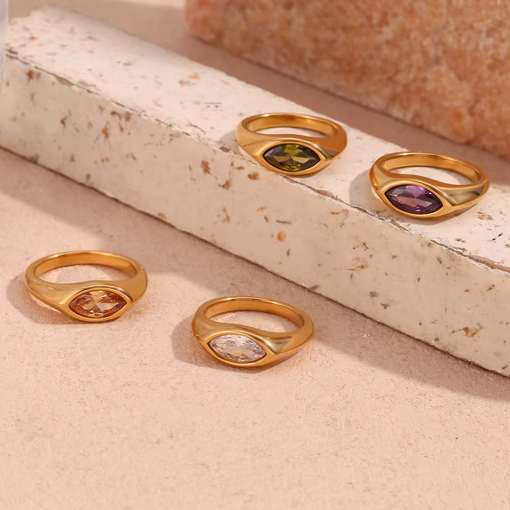 Four gold rings with gemstones on a textured surface