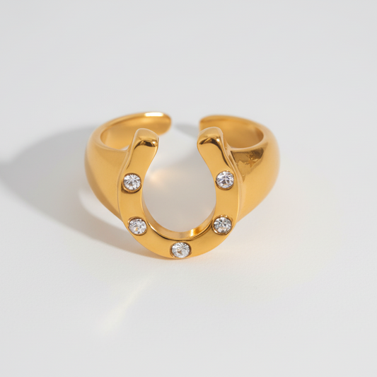 Gold horseshoe-shaped ring with embedded diamonds on a light gray background