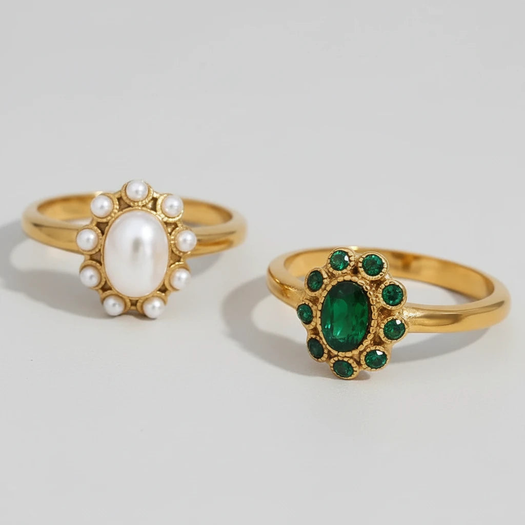 Two gold rings with pearls and emeralds on a light gray background