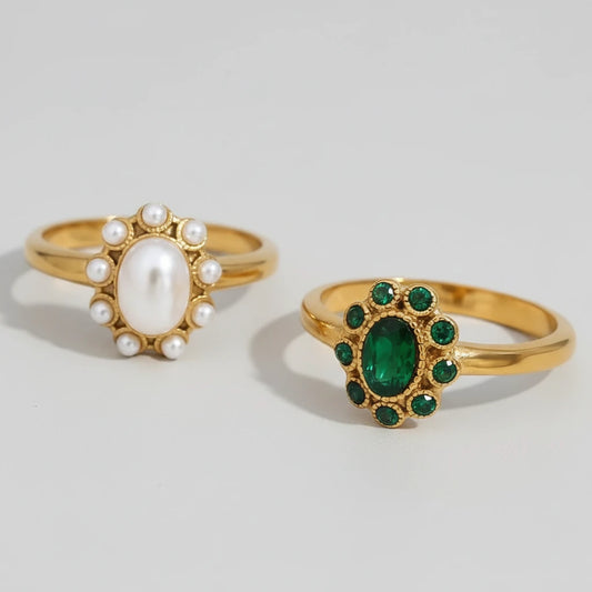 Two gold rings with pearls and emeralds on a light gray background